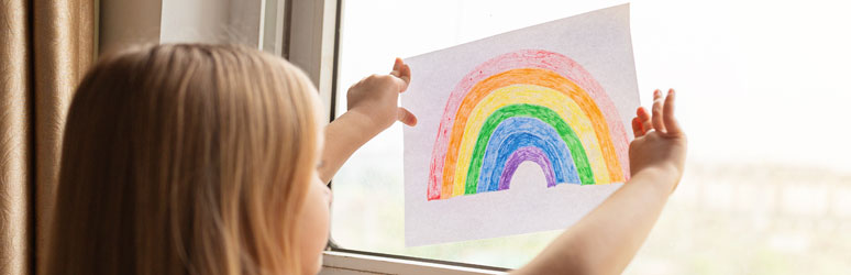 Kid putting rainbow drawing into window