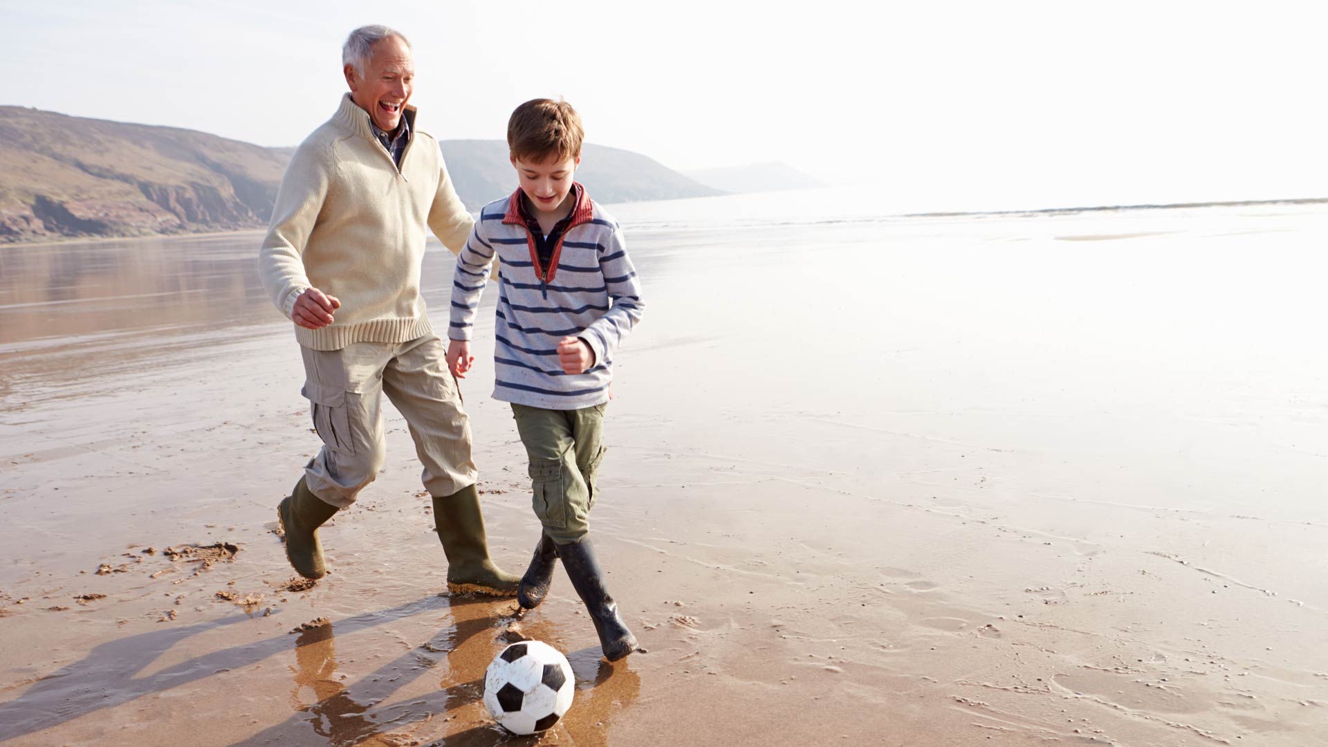 child and grandad playing football on the beach