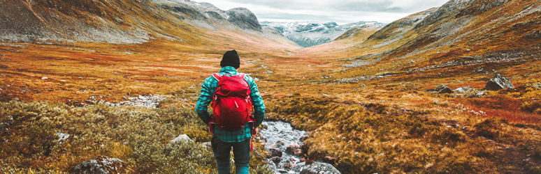 Man with a red backpack walking through valley in the autumn