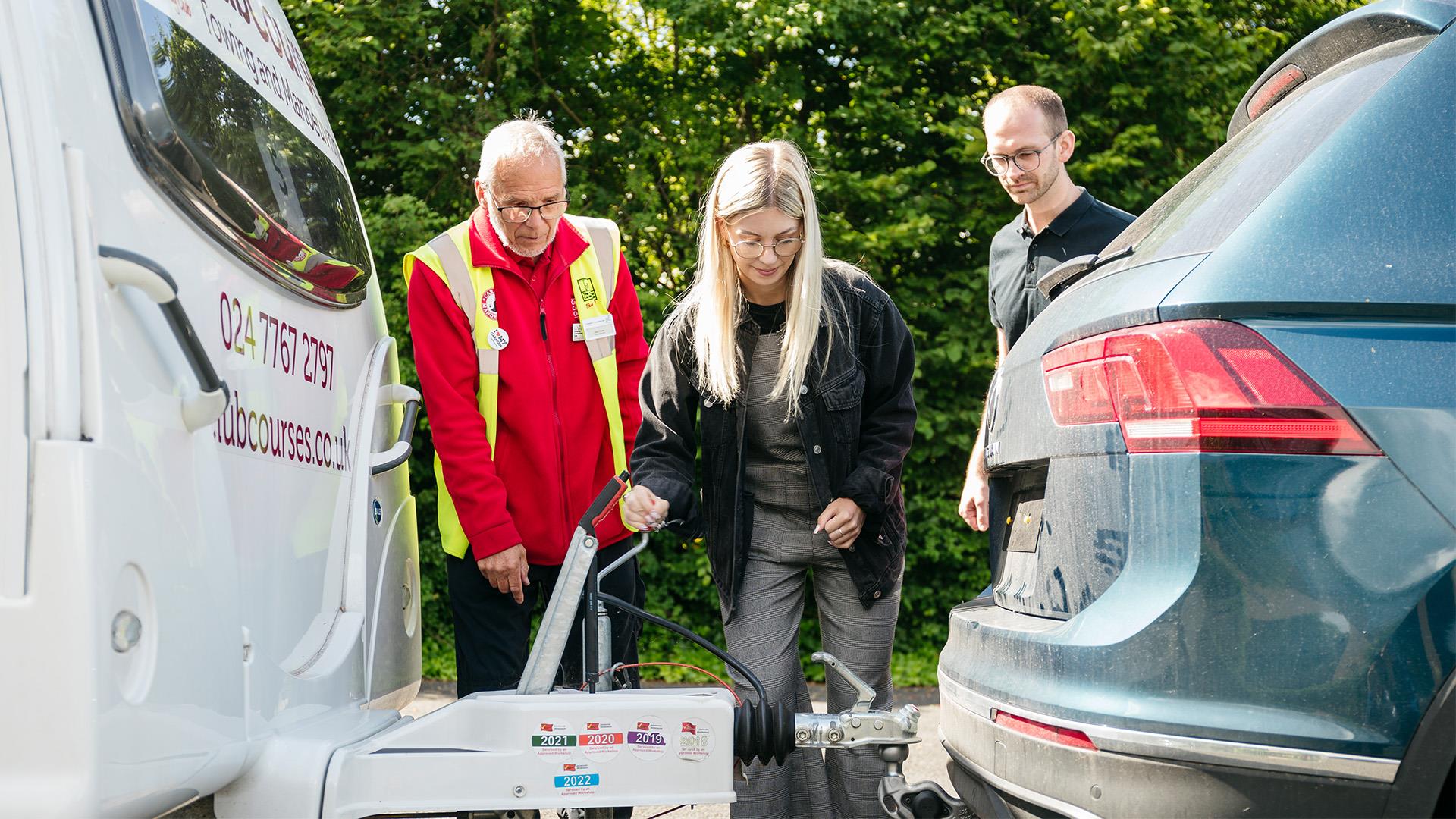 A couple stand with a towing expert next to a caravan