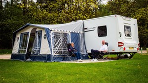 Couple sat in front of caravan with awning on Sherwood Pines campsite