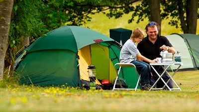 Dad and son enjoying a meal on their pop up stent and stool with tent in background