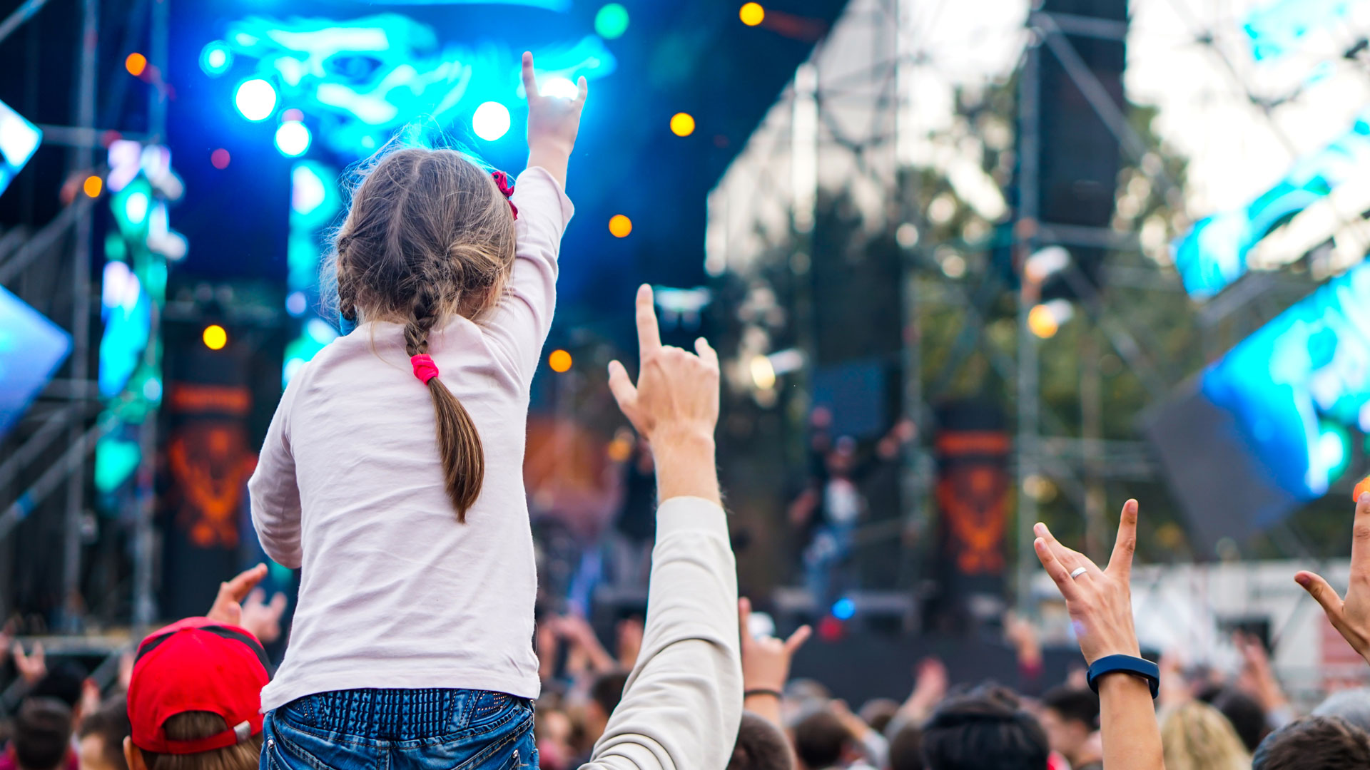 Girl sat on someone's shoulders at family music festival. 