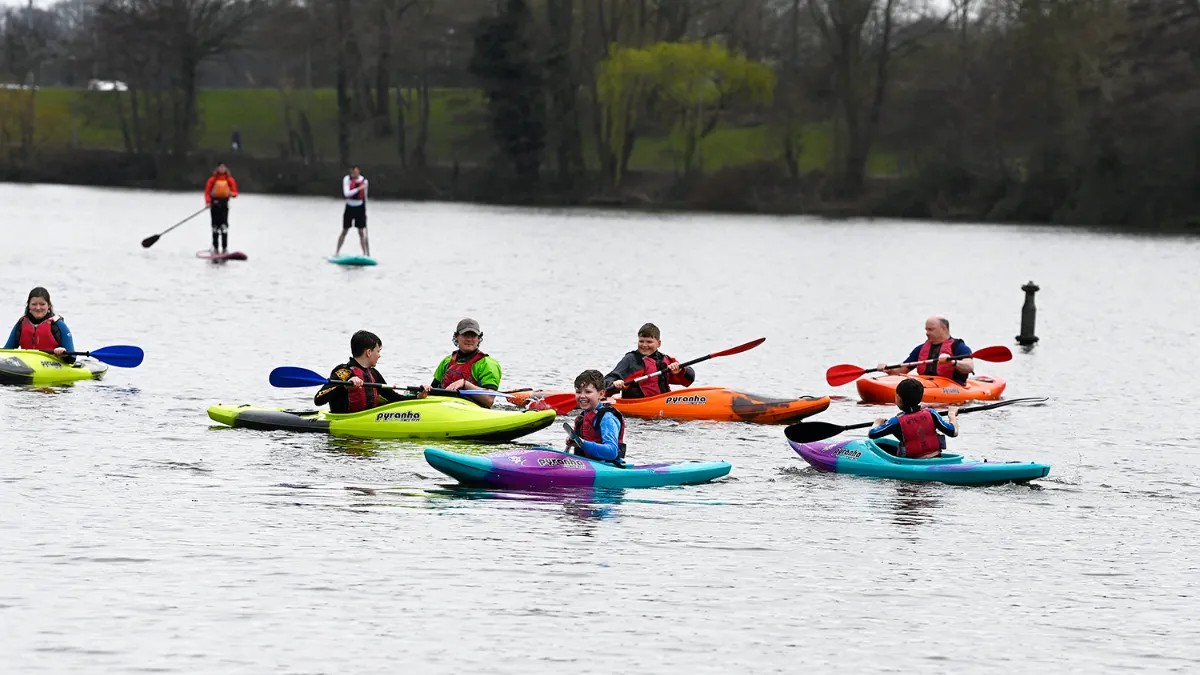 A group of people paddle brightly coloured kayaks along a river.