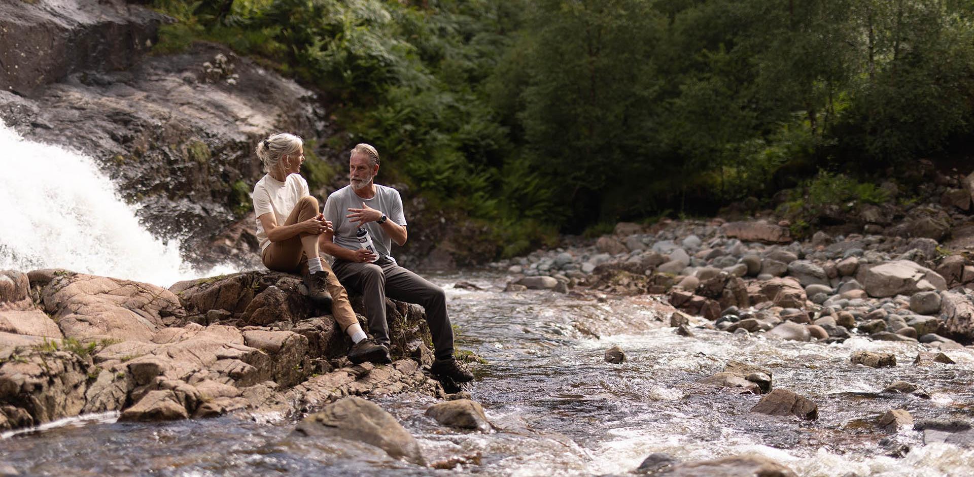 Man and woman resting on a rock by a fast moving shallow river