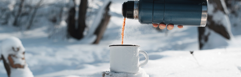 Pouring cofee into a mug from a flask with snow in the background