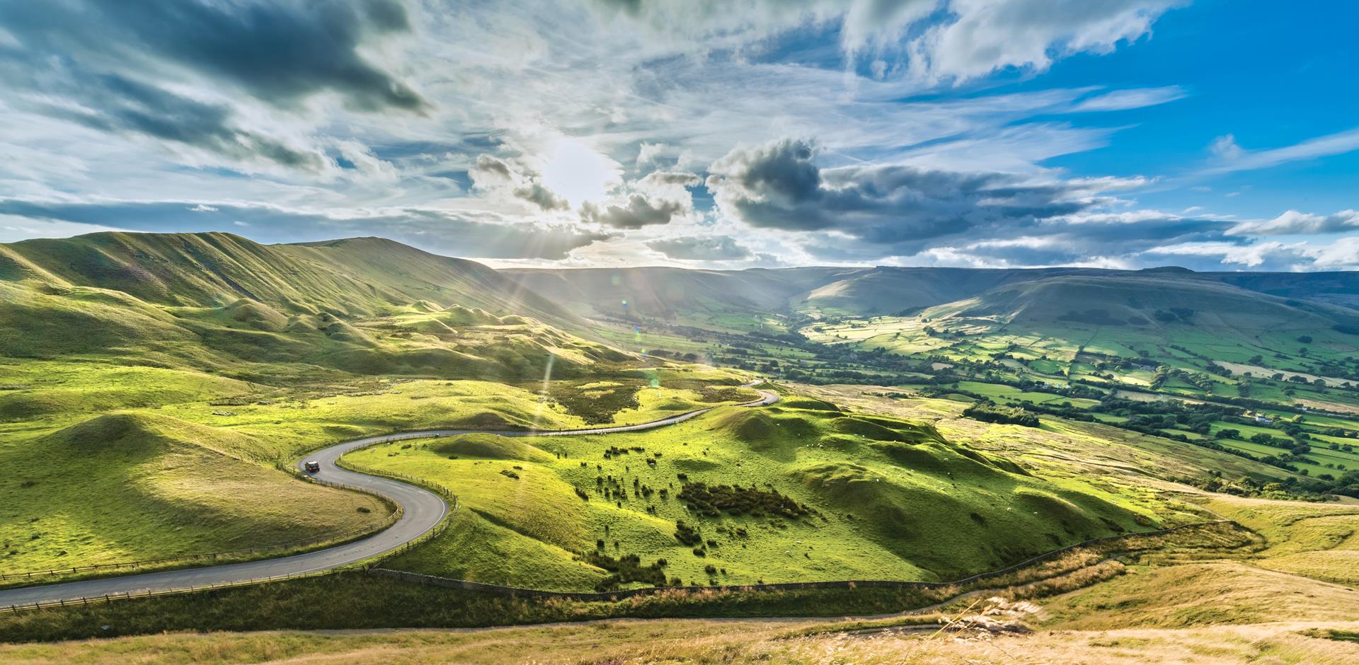 Serpentine Road among green hills of Peak District National Park, England.